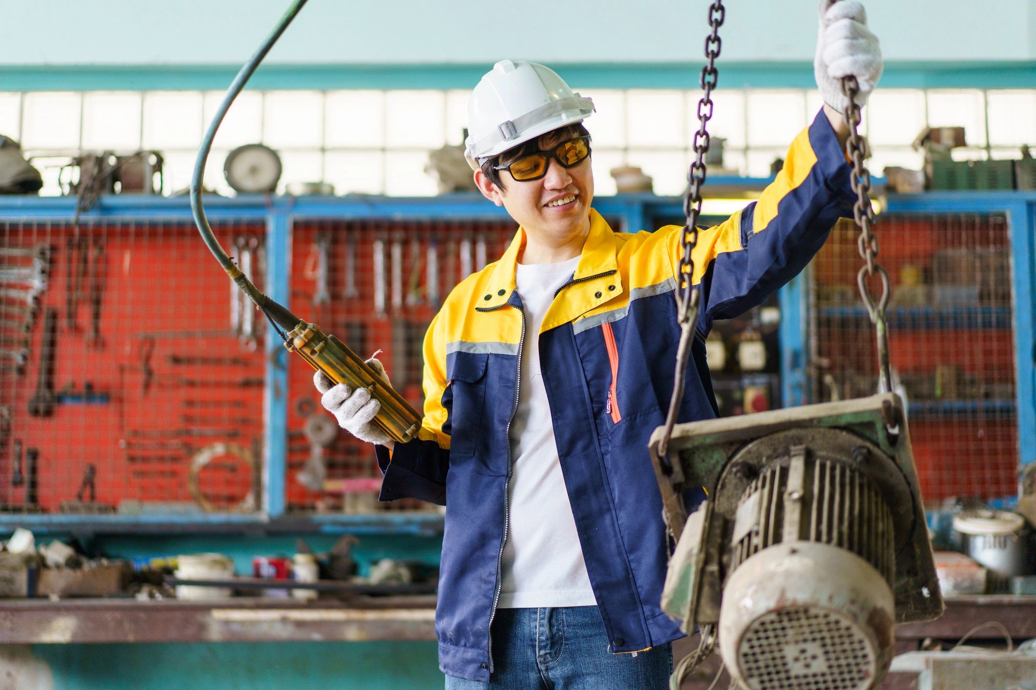Technician operating an overhead crane with a wired remote in a factory