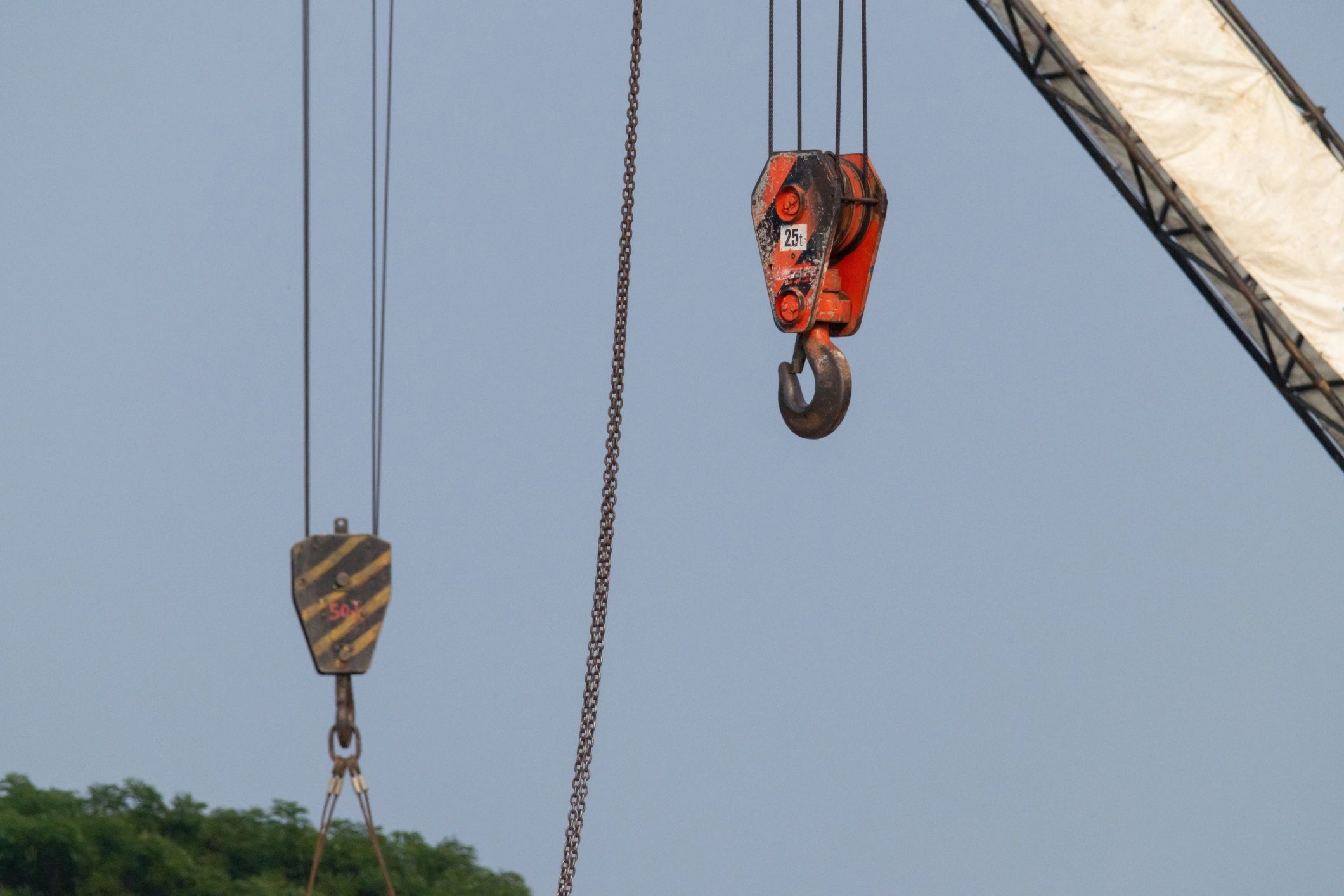 Heavy-duty crane hook and chains against a clear blue sky